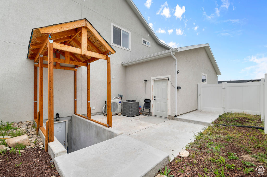 View of side of home with a gate, stucco siding, a patio, fence, and central AC unit