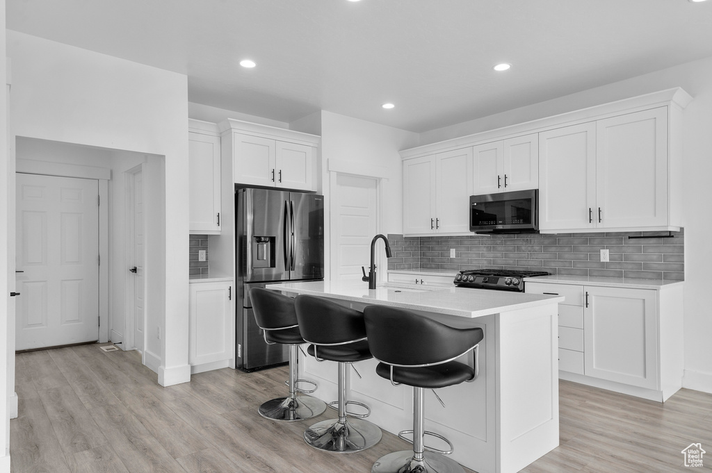 Kitchen with stainless steel appliances, a sink, light countertops, a kitchen breakfast bar, and white cabinets