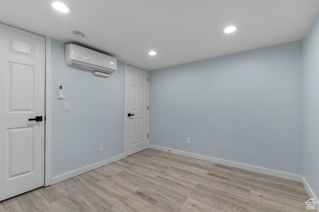 Unfurnished room featuring a wall unit AC, baseboards, light wood-style flooring, recessed lighting, and a smoke detector