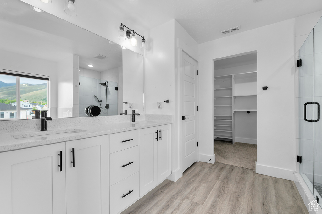 Bathroom featuring a shower stall, wood finished floors, double vanity, a walk in closet, and baseboards
