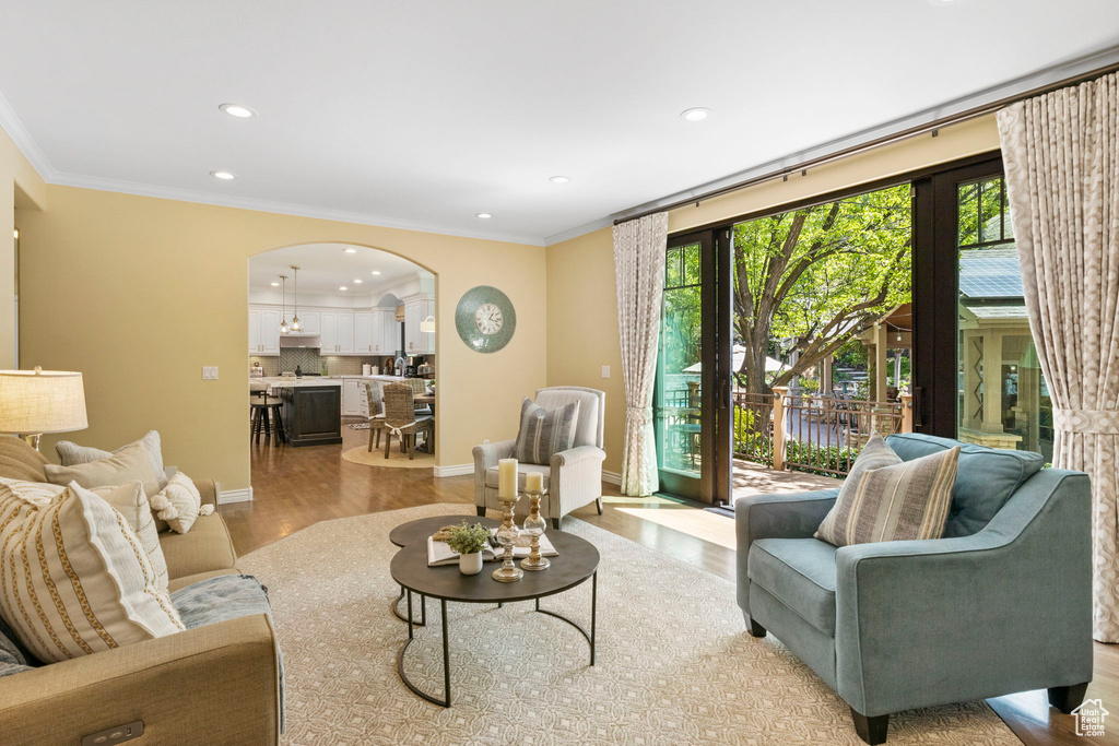 Living area with arched walkways, recessed lighting, light wood-style flooring, ornamental molding, and baseboards