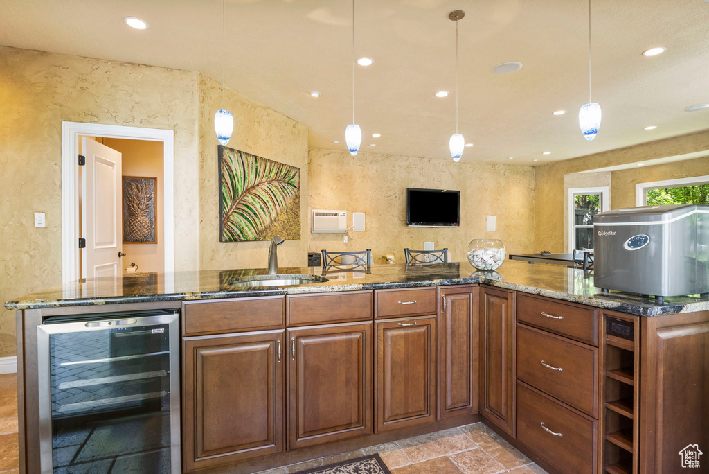 Kitchen featuring wine cooler, a sink, stone tile floors, a textured wall, and dark stone counters