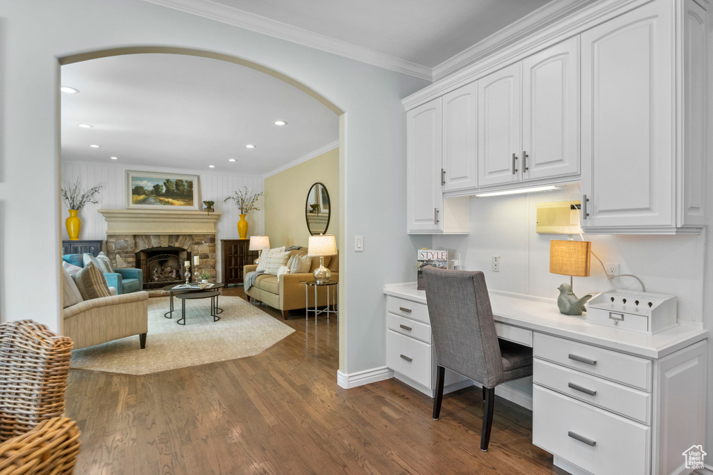 Office with arched walkways, built in desk, dark wood-type flooring, crown molding, and a stone fireplace