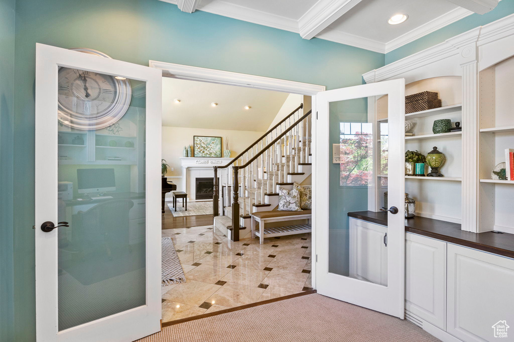 Foyer entrance with french doors, crown molding, beam ceiling, stairway, and a fireplace