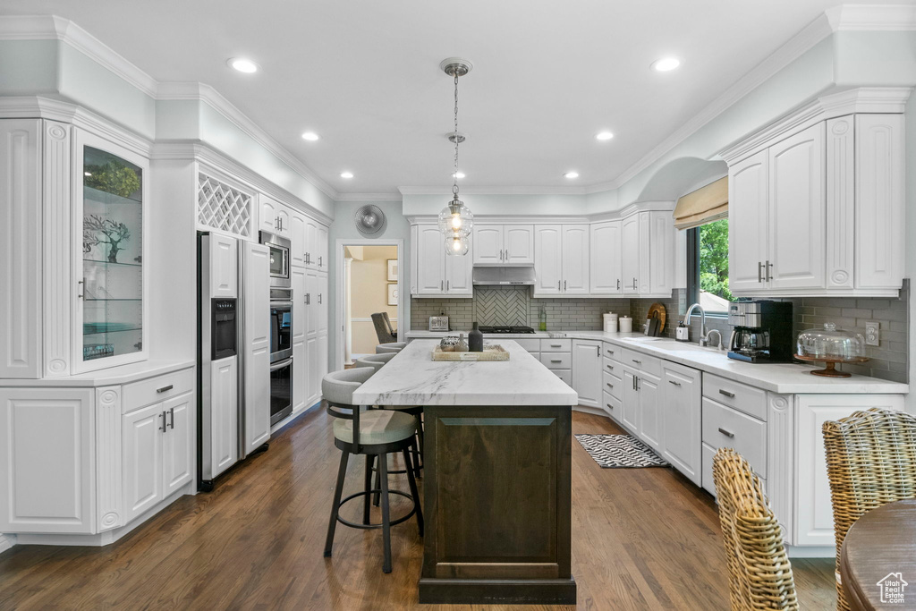 Kitchen featuring white cabinets, a sink, dark wood finished floors, a kitchen island, and a breakfast bar