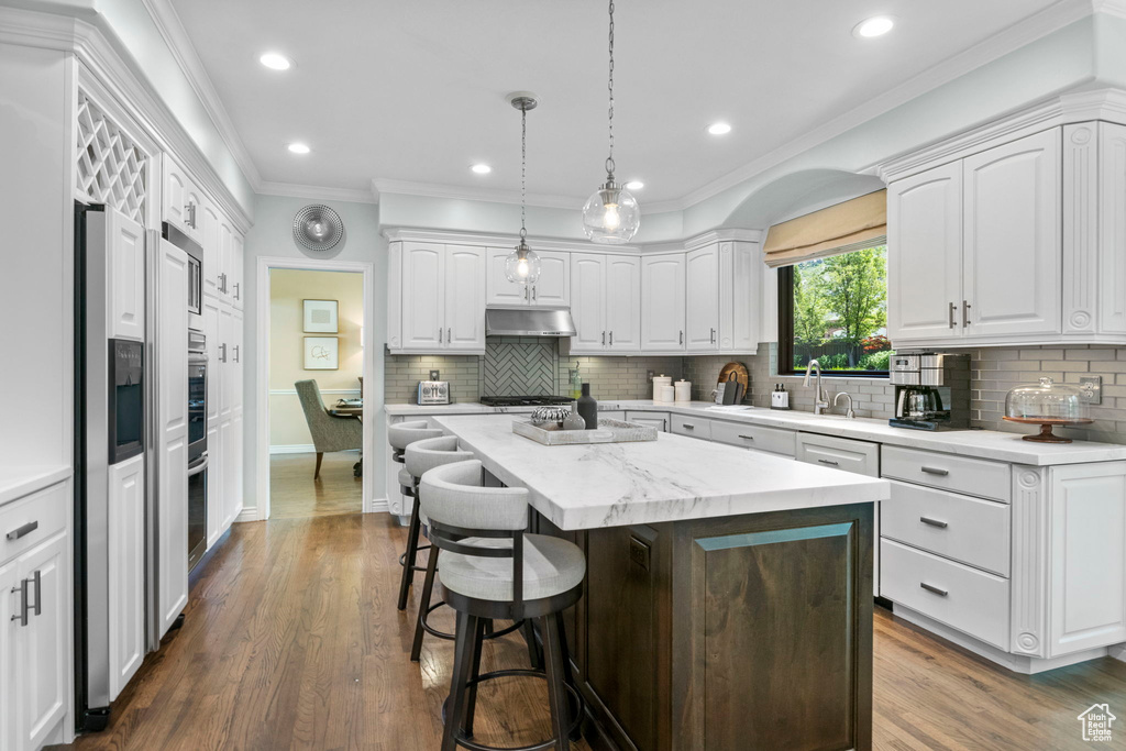 Kitchen featuring crown molding, white cabinets, a kitchen breakfast bar, under cabinet range hood, and a center island