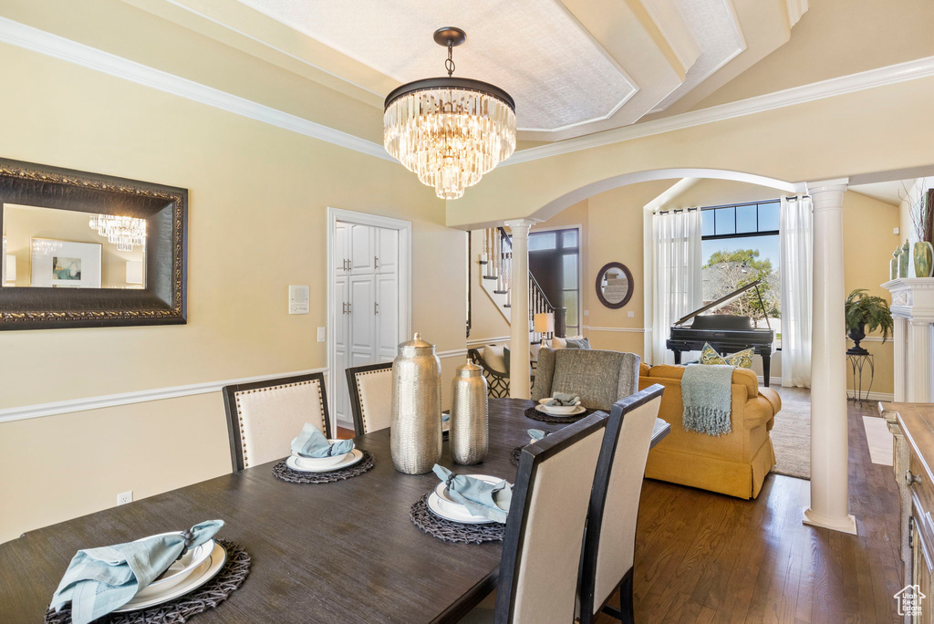 Dining space featuring ornate columns, arched walkways, a chandelier, crown molding, and wood finished floors