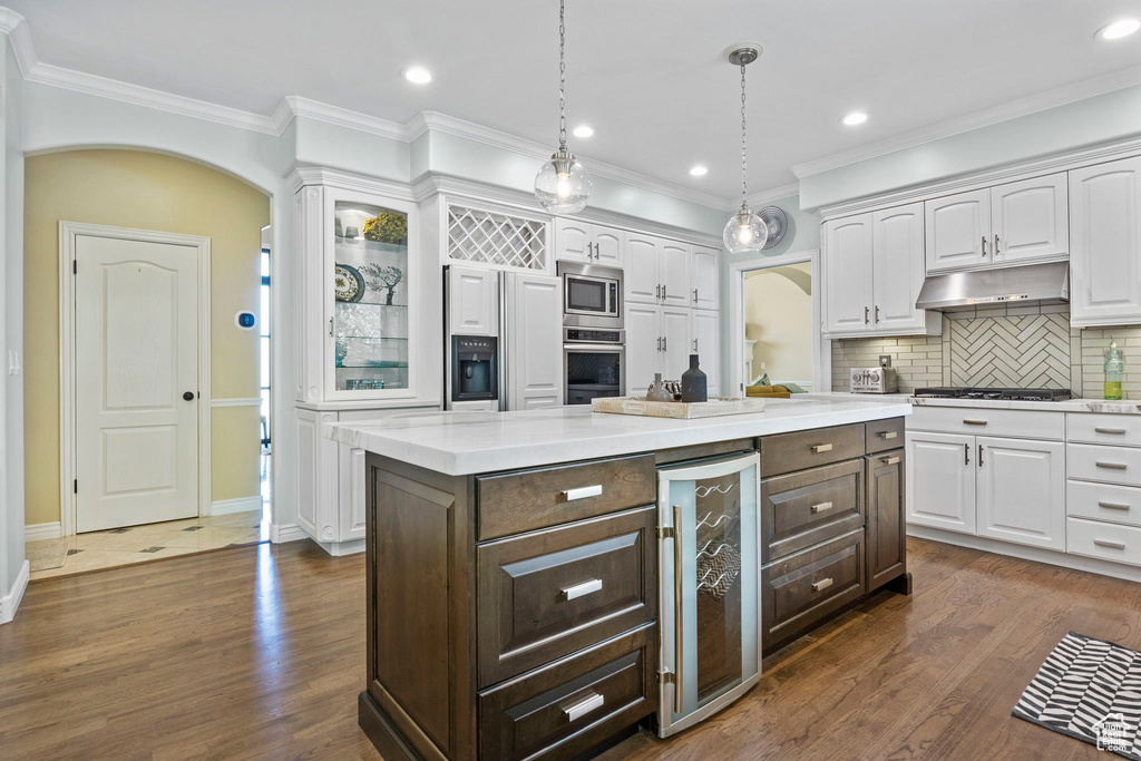 Kitchen with beverage cooler, appliances with stainless steel finishes, white cabinets, dark brown cabinetry, and tasteful backsplash
