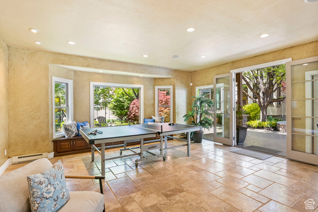 Recreation room with a baseboard heating unit, stone tile floors, recessed lighting, a textured wall, and french doors