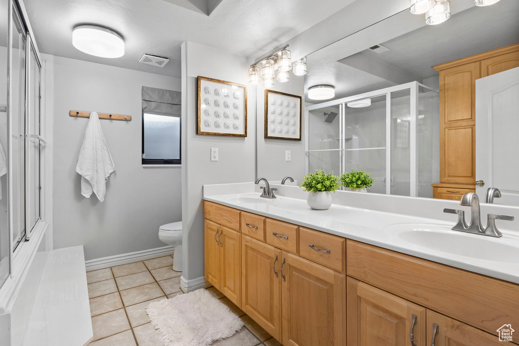 Full bath featuring a shower with door, tile patterned floors, toilet, double vanity, and baseboards