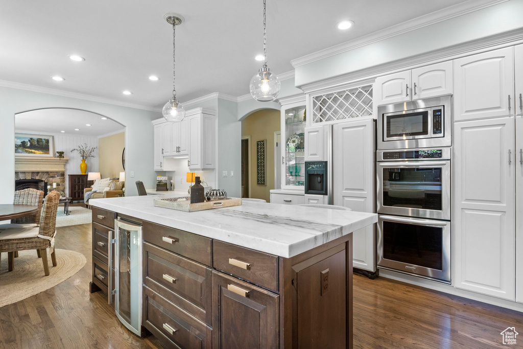 Kitchen with wine cooler, arched walkways, white cabinetry, crown molding, and a kitchen island