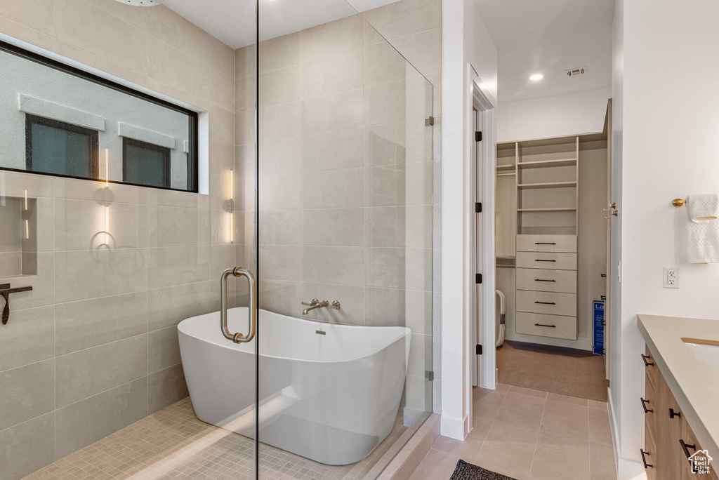 Bathroom featuring tile patterned floors, a spacious closet, a freestanding tub, tile walls, and tiled shower