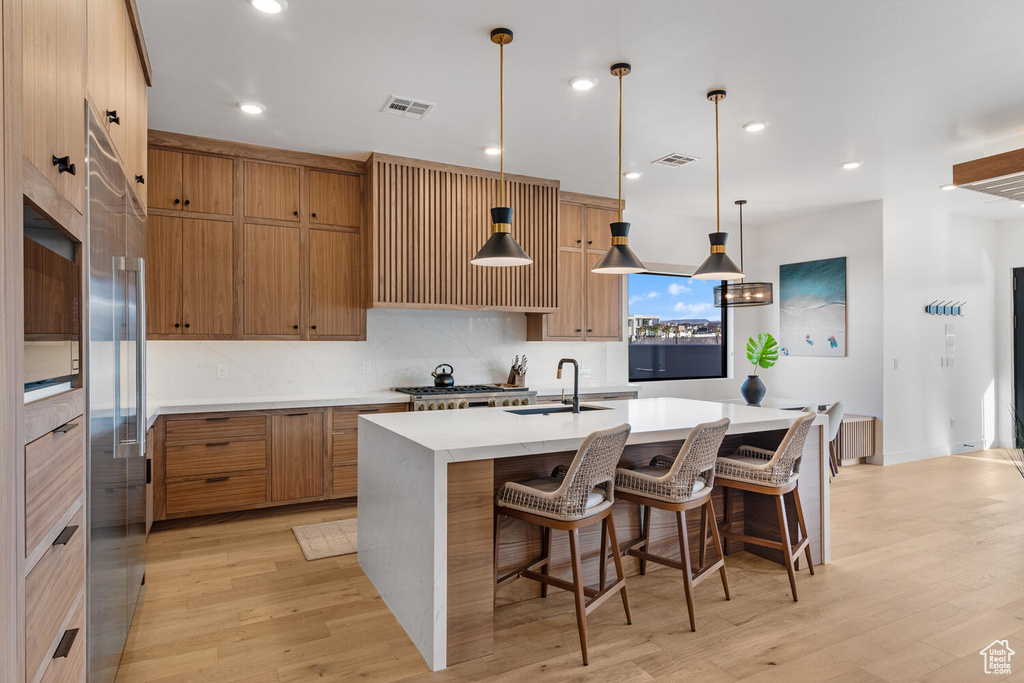 Kitchen featuring a sink, brown cabinets, a center island with sink, light wood-style flooring, and recessed lighting