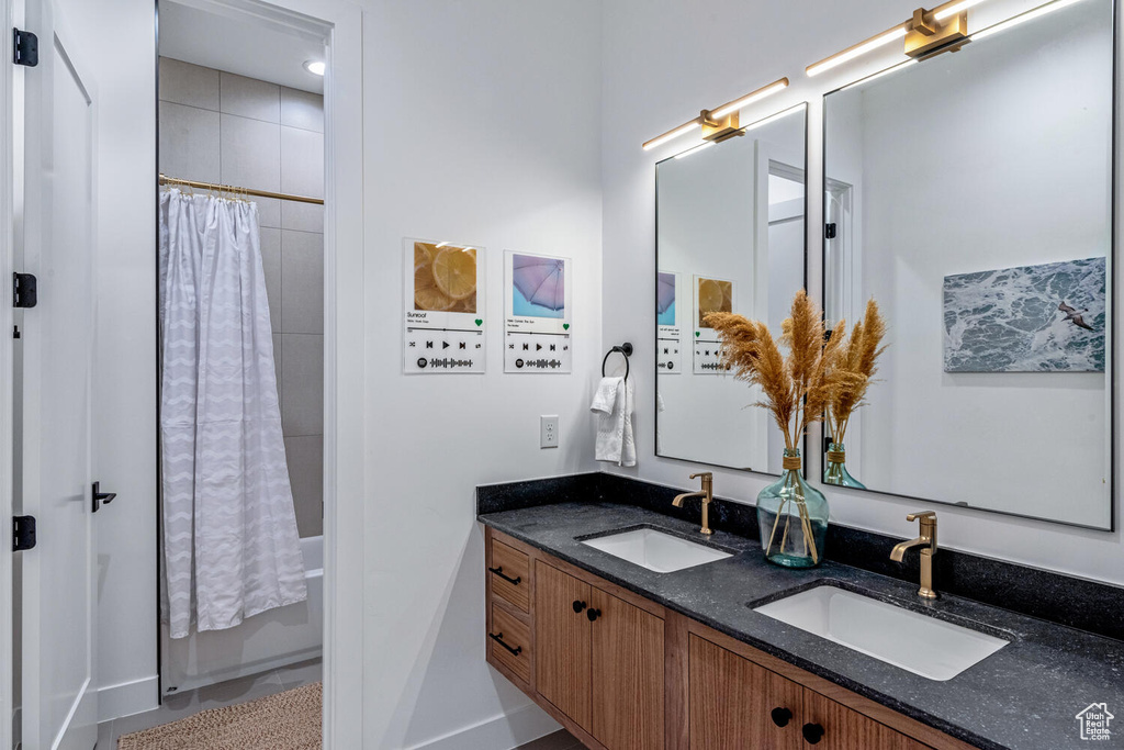 Bathroom featuring shower / tub combo with curtain, double vanity, and baseboards