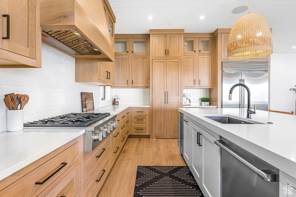 Kitchen with appliances with stainless steel finishes, custom range hood, light countertops, light wood finished floors, and recessed lighting