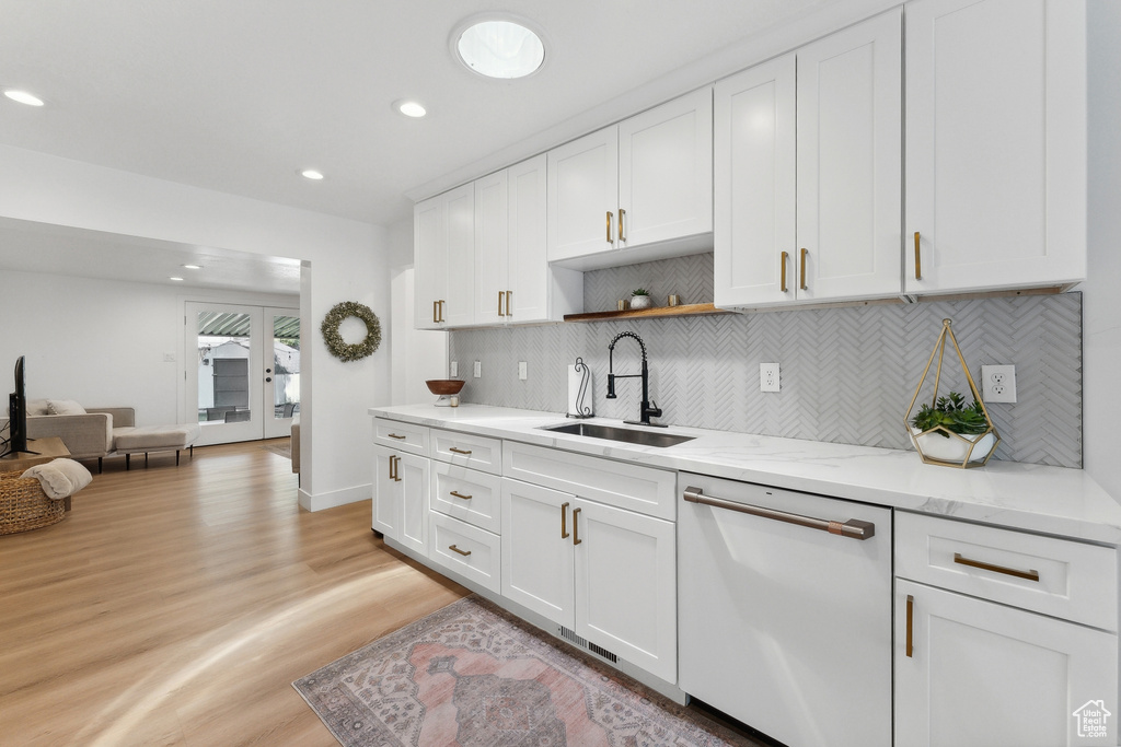 Kitchen featuring dishwasher, a sink, decorative backsplash, light wood-type flooring, and white cabinetry