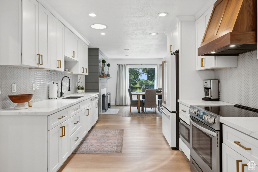 Kitchen featuring stainless steel electric stove, custom range hood, a sink, freestanding refrigerator, and light wood-style floors