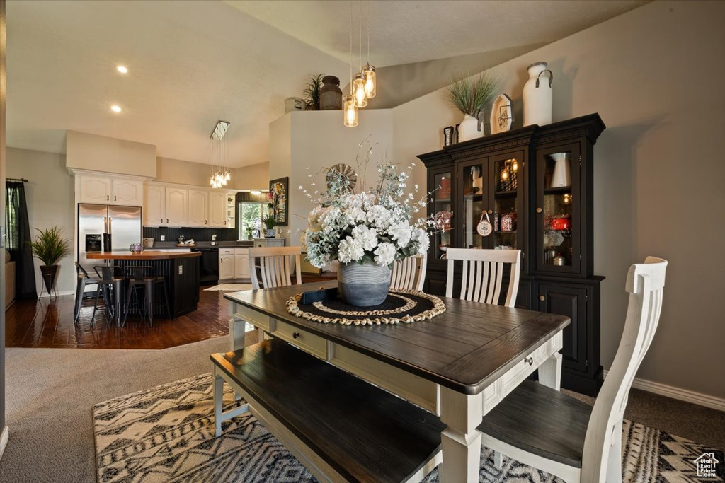 Dining room with a chandelier, vaulted ceiling, baseboards, and dark carpet