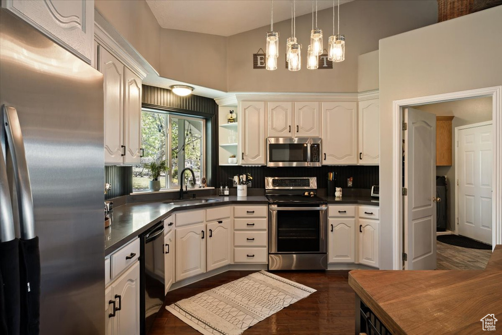 Kitchen featuring stainless steel appliances, a sink, dark countertops, white cabinets, and a high ceiling