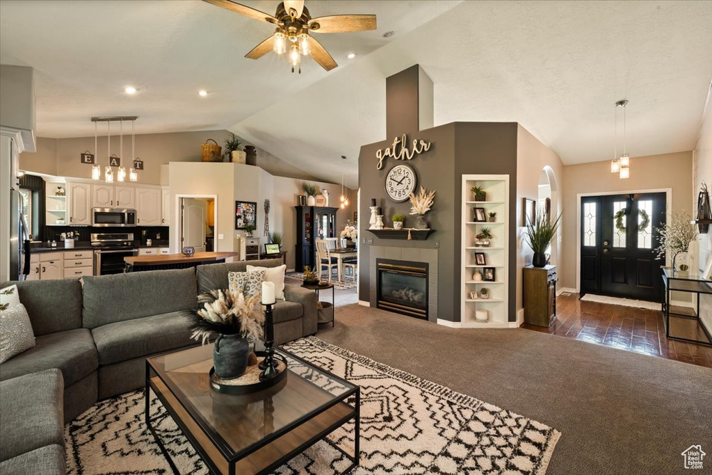 Living room featuring lofted ceiling, a ceiling fan, dark colored carpet, built in shelves, and baseboards