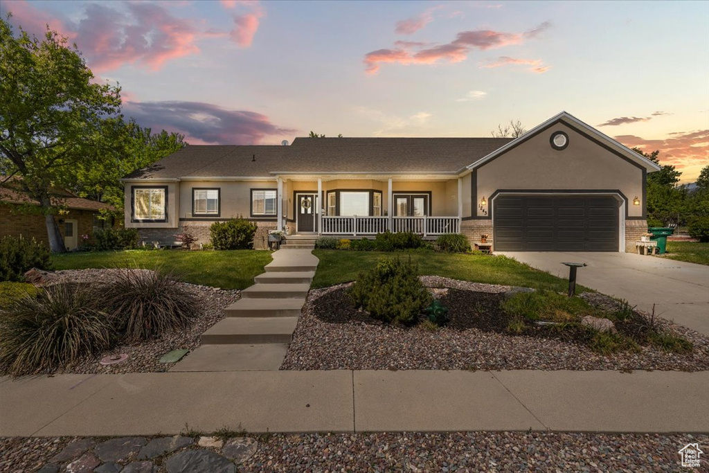 Single story home with covered porch, an attached garage, concrete driveway, stucco siding, and a lawn