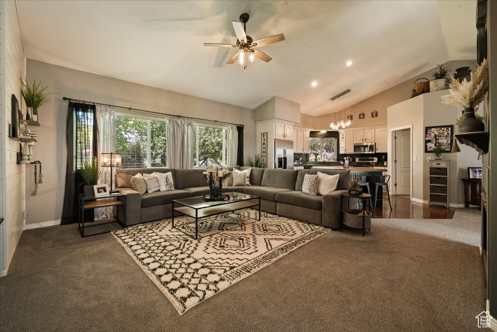 Living area with vaulted ceiling, ceiling fan, dark carpet, baseboards, and a chandelier