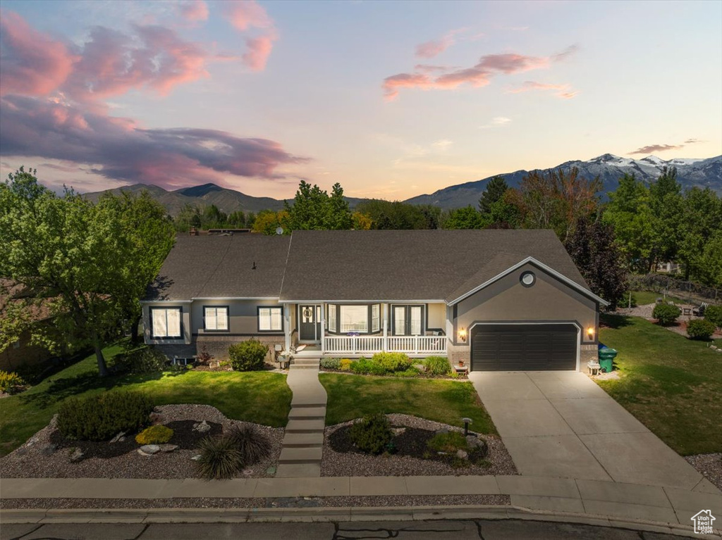 Single story home with covered porch, a mountain view, an attached garage, and a front lawn