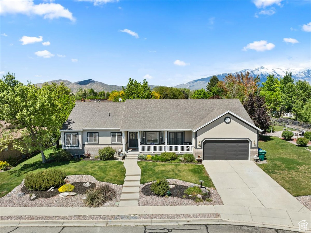 Ranch-style house with covered porch, a garage, a front yard, and a mountain view