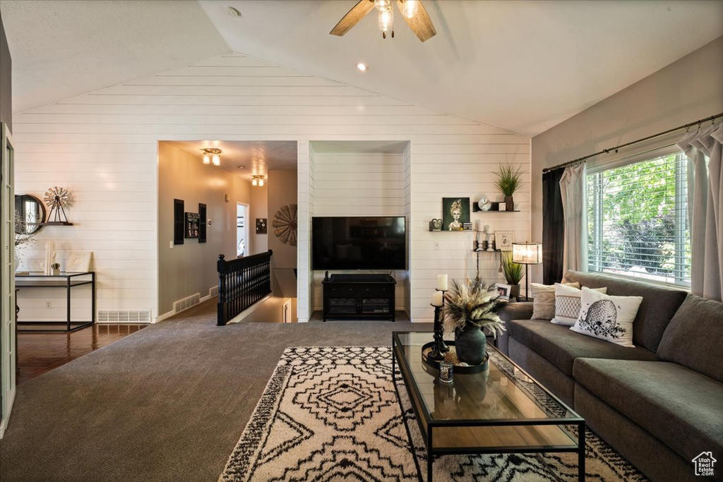 Carpeted living room with lofted ceiling, wooden walls, ceiling fan, and baseboards