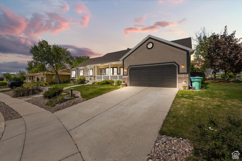 Ranch-style house with an attached garage, a lawn, driveway, a porch, and brick siding