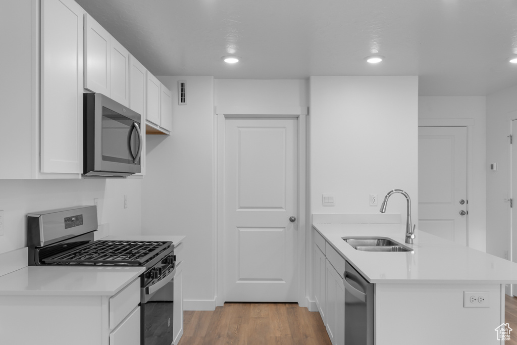 Kitchen with stainless steel appliances, a sink, a peninsula, light wood-style flooring, and light countertops