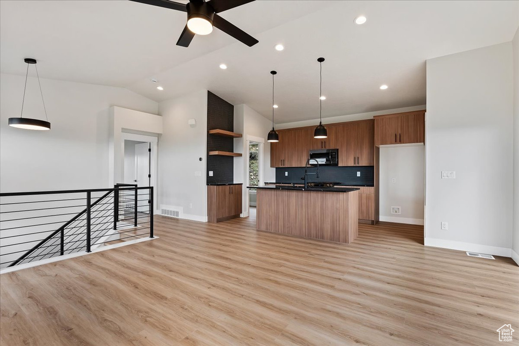 Kitchen with black microwave, open shelves, dark countertops, light wood-style flooring, and backsplash