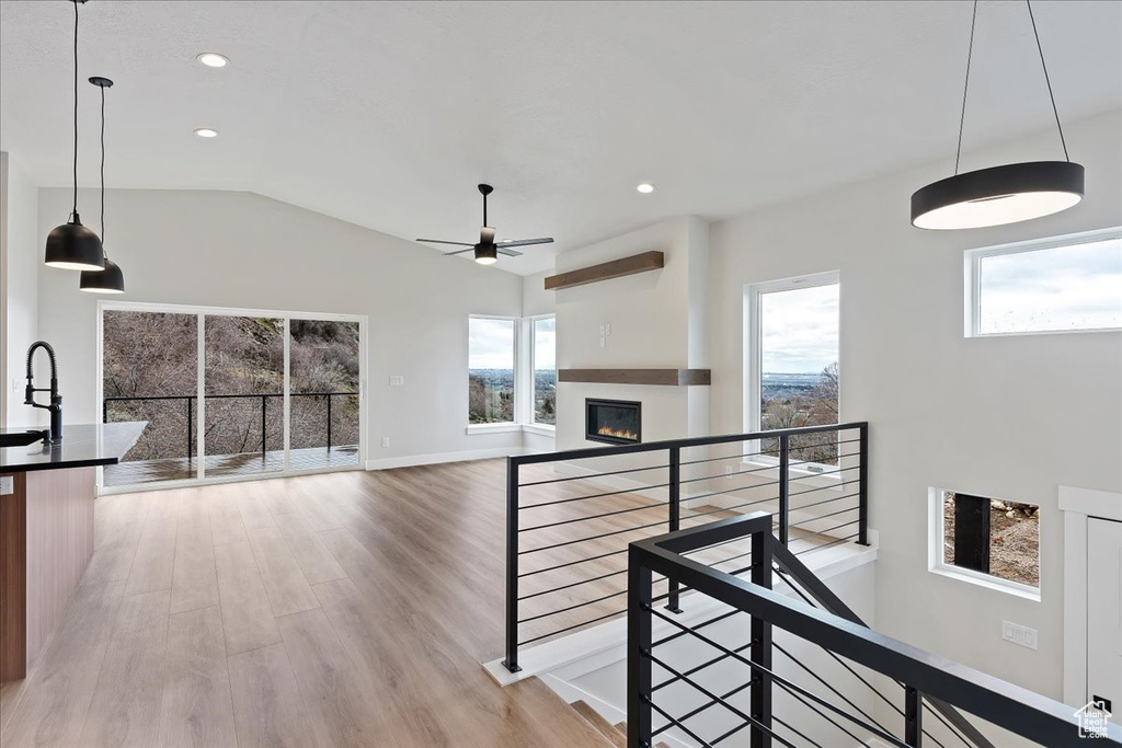 Stairway featuring plenty of natural light, a glass covered fireplace, wood finished floors, a ceiling fan, and vaulted ceiling