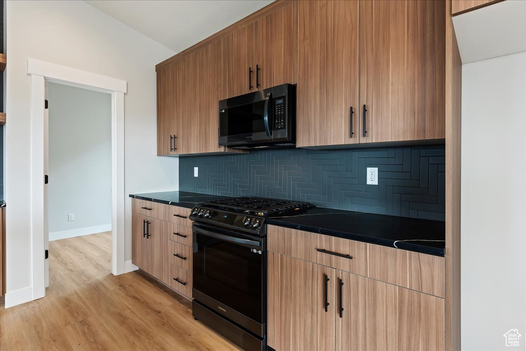 Kitchen with black gas stove, dark countertops, tasteful backsplash, light wood-style flooring, and baseboards