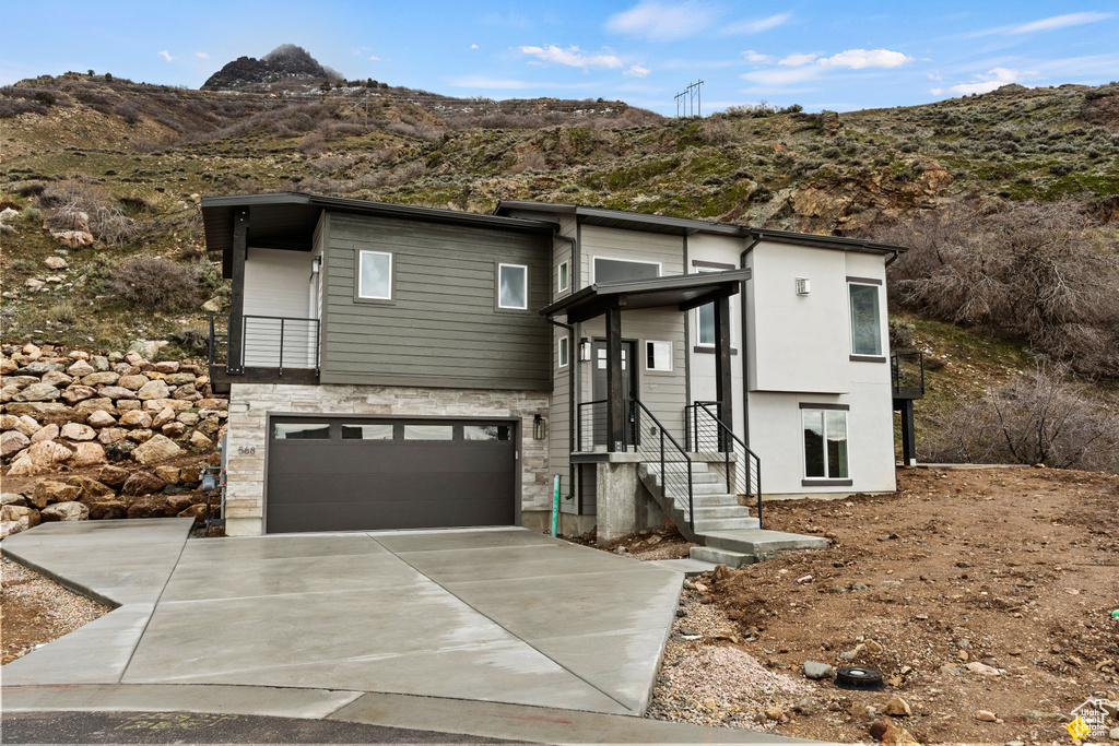Contemporary house featuring a mountain view, a garage, driveway, and stone siding