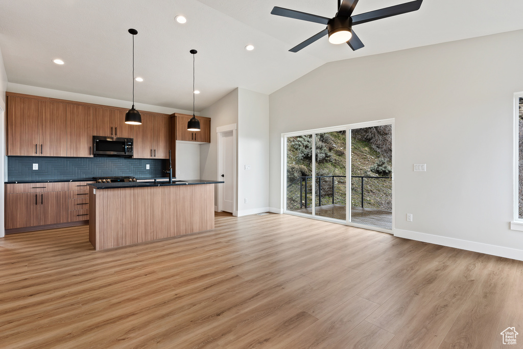 Kitchen with stainless steel microwave, dark countertops, decorative backsplash, open floor plan, and a ceiling fan