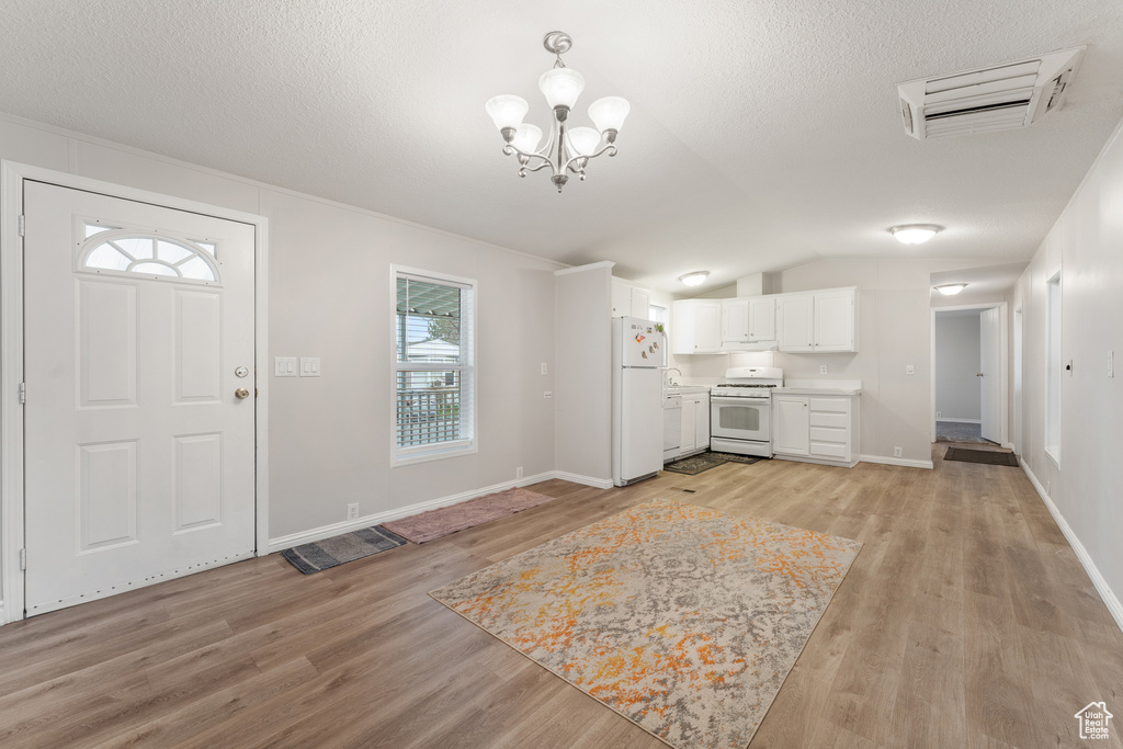 Interior space with light wood-type flooring, an inviting chandelier, a textured ceiling, visible vents, and lofted ceiling