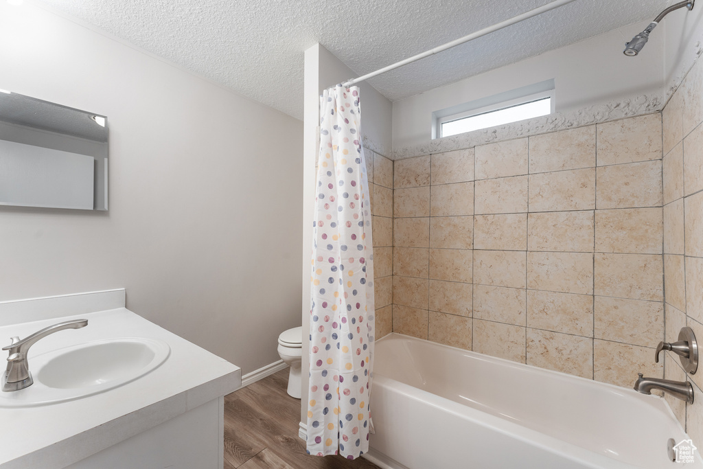 Bathroom featuring vanity, shower / tub combo with curtain, a textured ceiling, toilet, and wood finished floors