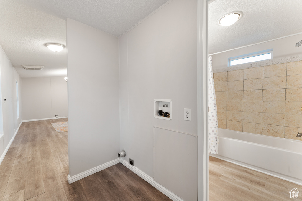 Clothes washing area with baseboards, a textured ceiling, visible vents, hookup for a washing machine, and wood finished floors