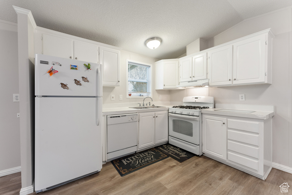 Kitchen featuring white cabinets, a sink, light countertops, white appliances, and under cabinet range hood