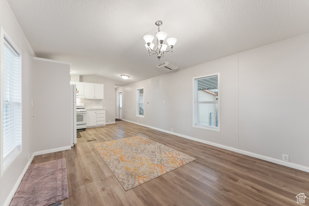 Unfurnished living room featuring light wood-style floors, a textured ceiling, vaulted ceiling, baseboards, and a notable chandelier