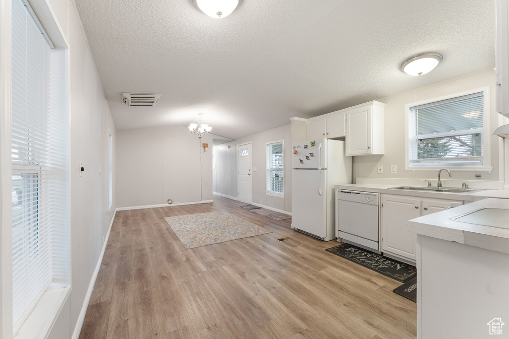 Kitchen with white appliances, light wood-style flooring, light countertops, a sink, and a notable chandelier
