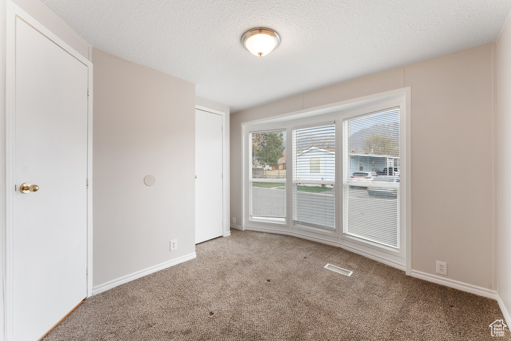 Empty room with a textured ceiling, visible vents, baseboards, and carpet