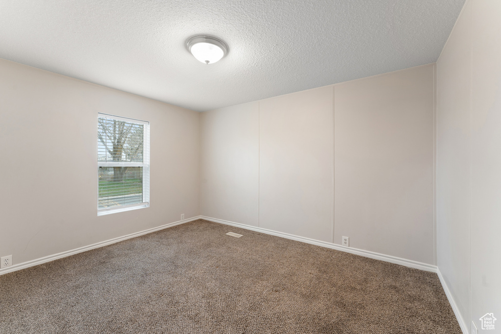 Carpeted empty room featuring a textured ceiling and baseboards