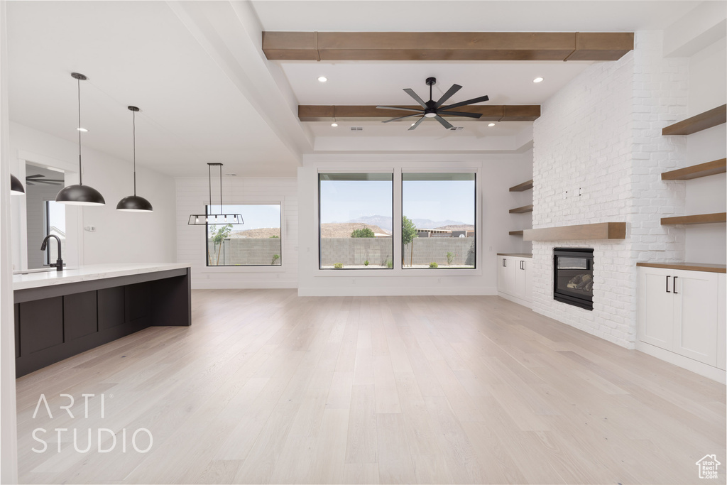 Unfurnished living room with a fireplace, a ceiling fan, light wood-style floors, beam ceiling, and a sink