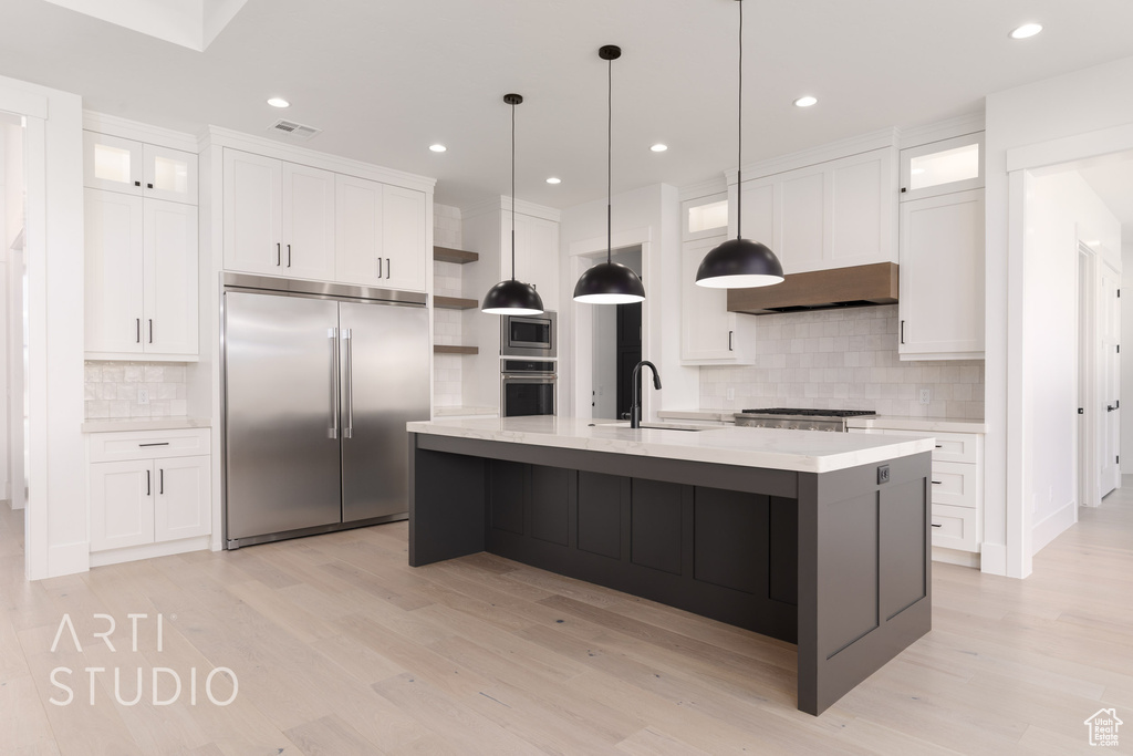 Kitchen featuring built in appliances, open shelves, wall chimney range hood, backsplash, and light wood-style flooring