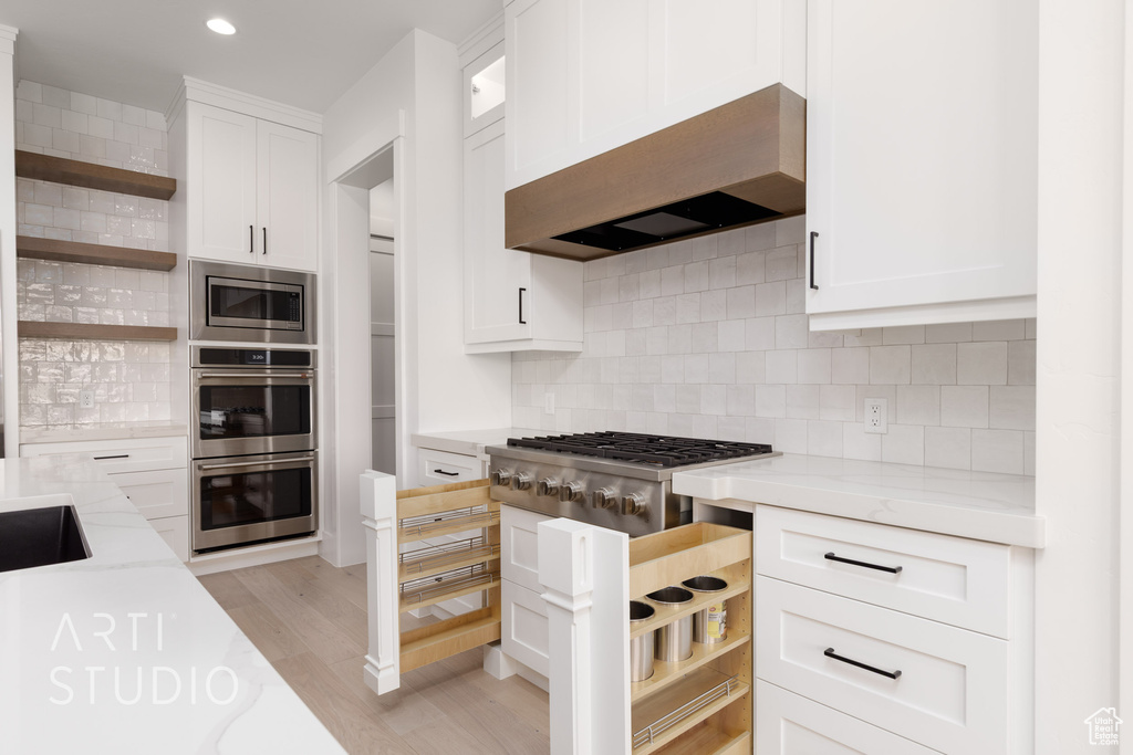 Kitchen with open shelves, stainless steel appliances, wall chimney exhaust hood, light stone counters, and white cabinets