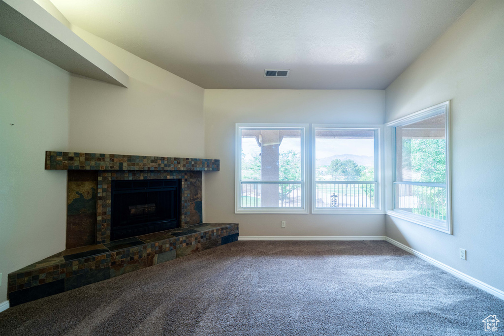 Unfurnished living room featuring healthy amount of natural light, baseboards, carpet flooring, and a fireplace with raised hearth
