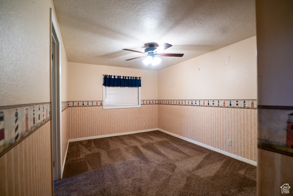 Carpeted spare room with ceiling fan, a wainscoted wall, and a textured ceiling