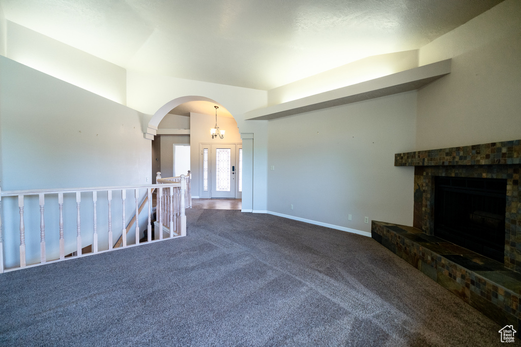 Unfurnished living room with carpet floors, a fireplace with raised hearth, arched walkways, and baseboards